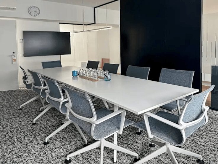 Besprechungsraum mit großem Tisch, Stühlen und Bildschirm an der Wand